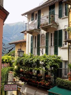 an apartment building with green shutters and balconies on the balcony, in front of mountains