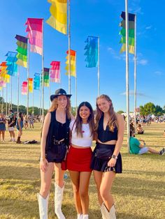 three young women standing next to each other on top of a grass covered field with flags in the background