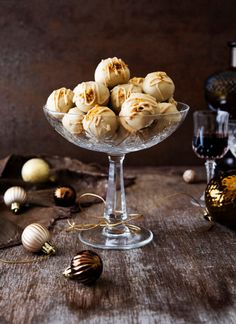 a glass bowl filled with cookies on top of a wooden table next to wine glasses