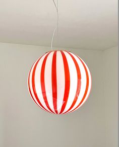 a red and white striped ball hanging from a ceiling fixture in a room with gray walls