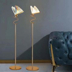 two floor lamps sitting next to each other on top of a white floor in front of a blue chair