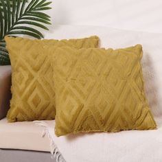 two yellow pillows sitting on top of a white couch next to a potted plant