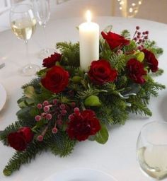 red roses and greenery are arranged on a table with two white candles in the center