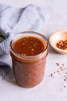 a glass jar filled with chili sauce next to a wooden spoon and striped dish towel