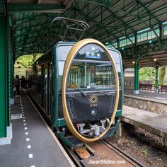 a green and yellow train parked at a station with its reflection in it's mirror