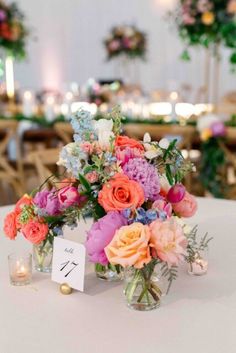 a vase filled with lots of colorful flowers on top of a white table covered in candles