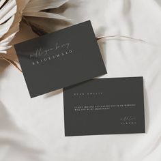 two black and white business cards sitting on top of a bed next to some flowers