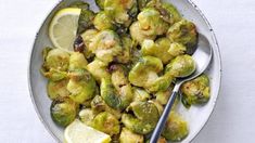 a white bowl filled with brussel sprouts and lemon wedges next to a fork