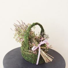 a basket filled with grass and flowers on top of a black round table next to a white wall