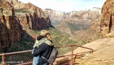 a man and woman standing at the edge of a cliff looking out over a valley