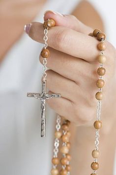 a woman holding a rosary with a cross hanging from it's middle finger and wearing a white shirt