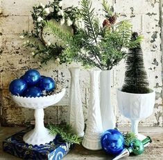 three white vases filled with blue ornaments and greenery on top of a table