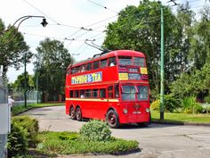 a red double decker bus driving down a street next to power lines and green trees