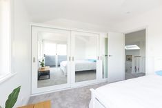 a bedroom with white walls and doors leading to a bed room that has a large mirror on the wall