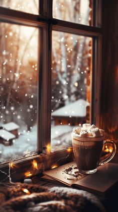 a cup of coffee sitting on top of a window sill next to a snow covered forest