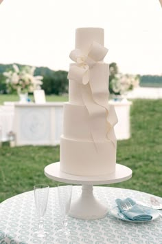 a white wedding cake sitting on top of a table in front of a green field