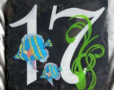 two fish painted on a slate block with the number seven in white and green paint