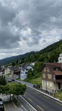 a street with cars parked on both sides and houses in the distance under a cloudy sky