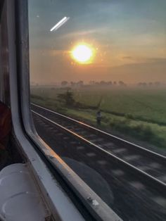 the sun is setting over an open field as seen from inside a train car window