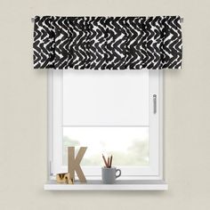 a black and white patterned roman blind with the letter k on it next to a cup