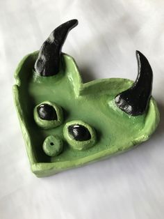 a green ceramic object with black horns and eyes