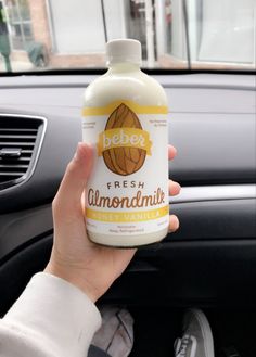 a person holding up a bottle of almond milk in their hand while sitting in the driver's seat of a car