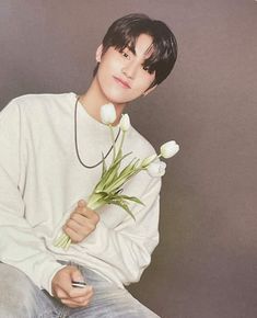 a young man sitting down holding flowers in his hand and looking at the camera with an intense look on his face