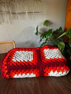 a red and white crocheted blanket sitting on top of a wooden table next to a potted plant