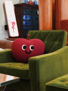 an apple pillow sitting on top of a green chair next to a table and lamp