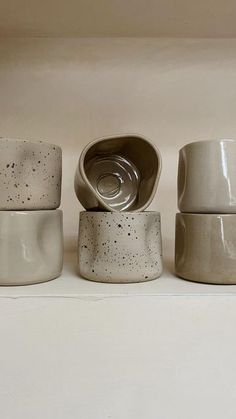 three bowls and one cup are sitting on the shelf next to each other in front of a white wall