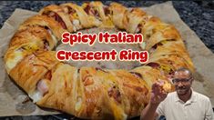 a man holding a piece of food in front of a large pastry ring with meat and cheese on it