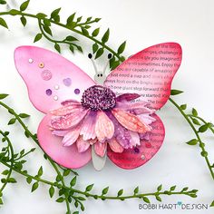 a pink and purple butterfly sitting on top of a green twig with leaves around it