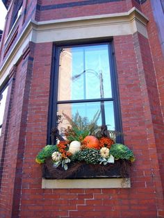 a window box with pumpkins, gourds and greenery in front of a brick building