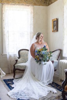 a woman in a wedding dress sitting on a chair holding a bouquet and smiling at the camera