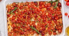 a square casserole dish with tomatoes and herbs on it, surrounded by olives