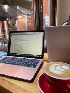 a laptop computer sitting on top of a wooden table next to a cup of coffee