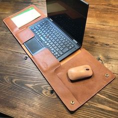 an open laptop computer sitting on top of a brown leather case next to a mouse