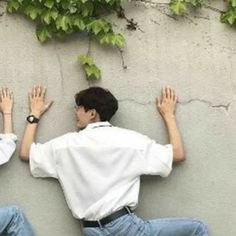 two young men sitting against a wall with their hands in the air