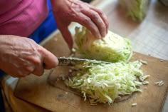 a person cutting cabbage on top of a wooden cutting board