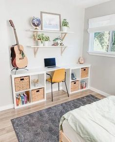 a bedroom with a bed, desk and guitar on the wall next to bookshelves