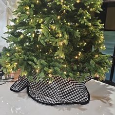 a small christmas tree in a black and white basket with lights on the top is sitting on a table