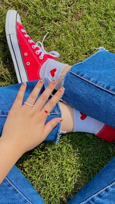 a woman's hand with red nail polish sitting on the grass next to her jeans