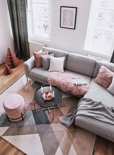 a living room with grey couches and pink pillows on the coffee table in front of it