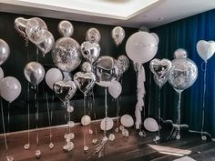 balloons and streamers are hanging from the ceiling in front of a black wall with blue drapes