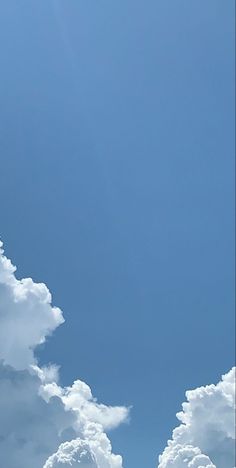 the airplane is flying high in the blue sky with white clouds above it and below