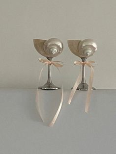 two silver candlesticks with bows on them sitting next to each other in front of a white wall