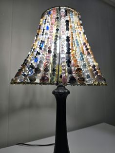 a lamp made out of glass beads on a black stand with a white wall in the background