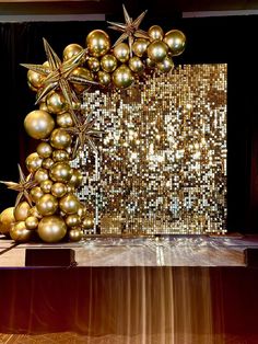 a table topped with lots of gold balloons next to a wall covered in sequins