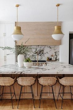 a kitchen with marble counter tops and gold pendant lights hanging over the island in front of it