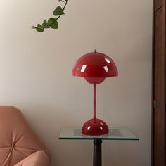 a red lamp sitting on top of a glass table next to a pink chair and potted plant